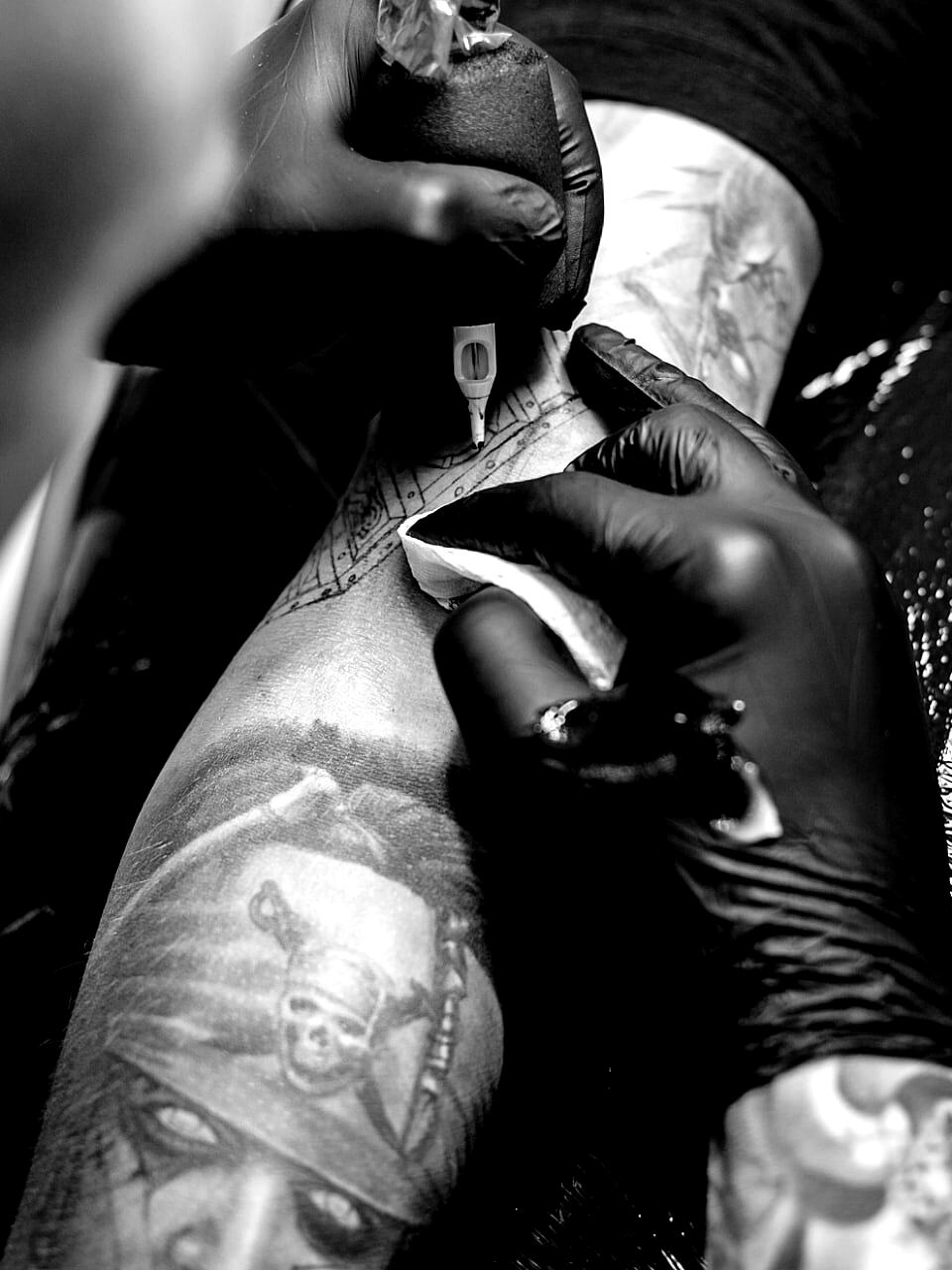 Mains gantées tenant une machine à tatouer au-dessus d'un avant-bras en cours de tatouage