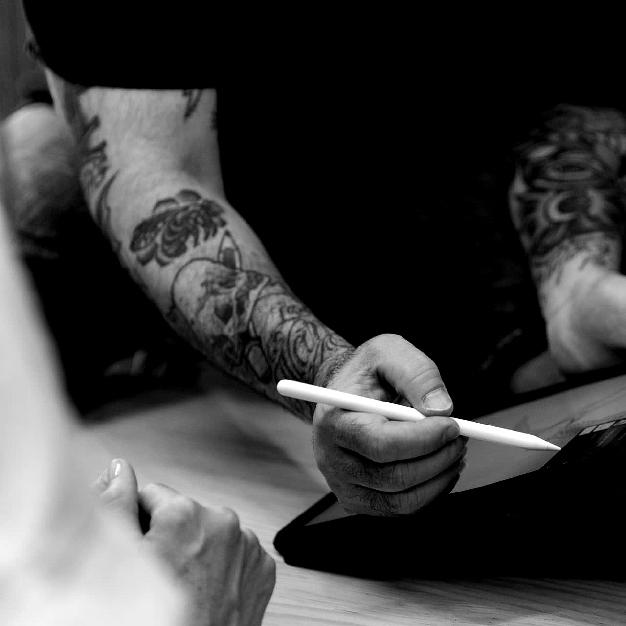 Avant-bras tatoués tenant un stylet au-dessus d'une tablette graphique posée sur les genoux