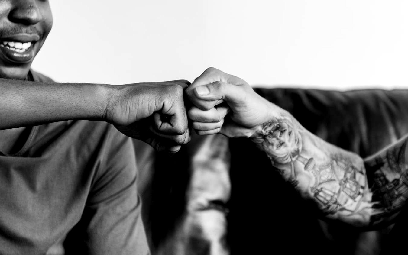 Deux personnes se tapent le poing, l'un des bras est entièrement tatoué