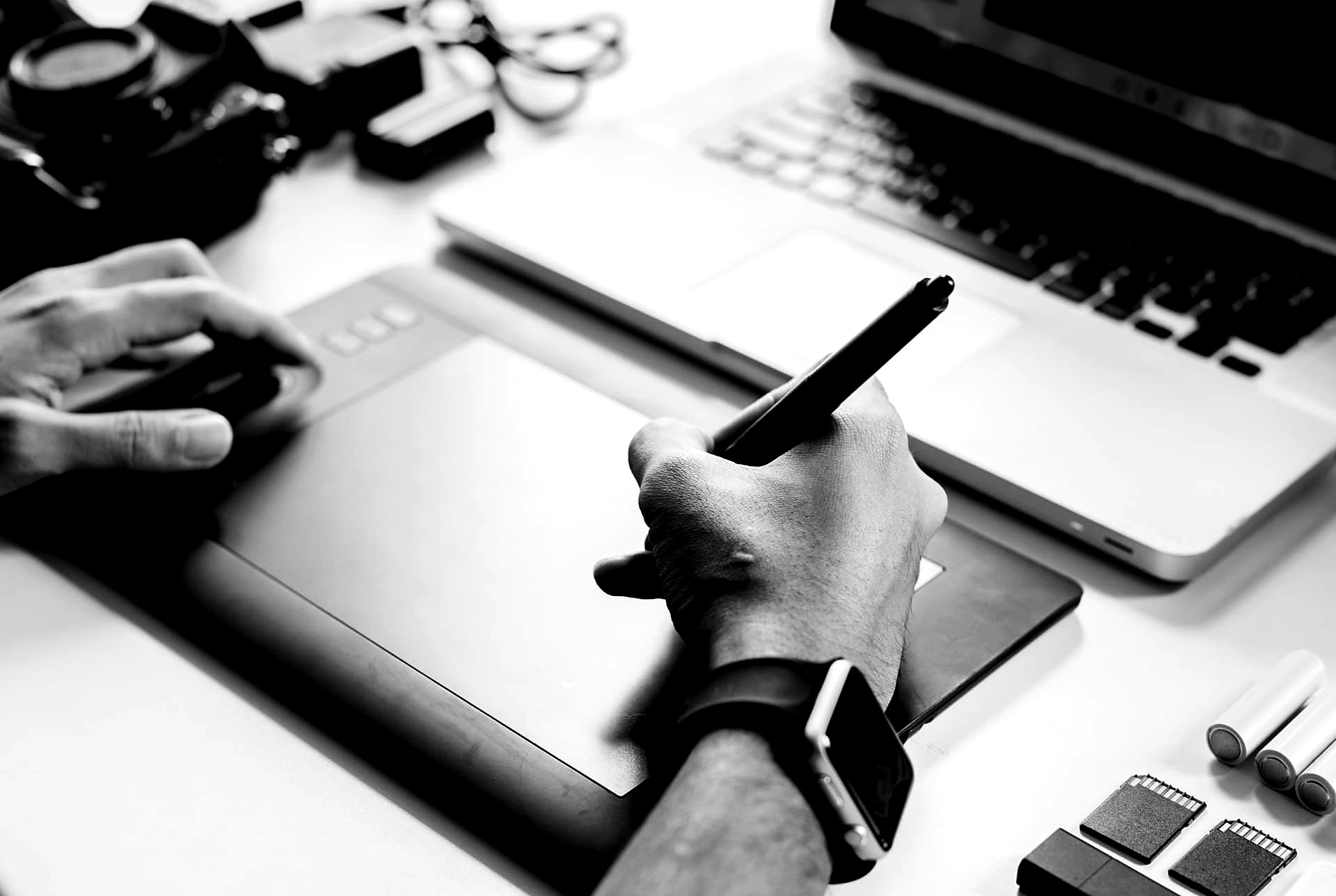 Bureau clair vu de dessus : main tenant un stylet sur une tablette graphique, ordinateur portable et appareil photo